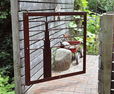 A small rusty garden gate with a wheelbarrow nearby depicting the metal gate issues.